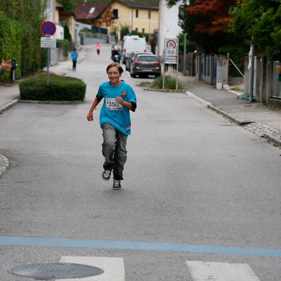 Ein junger Junge mit einem blauen Shirt mit der Nummer 350 läuft auf einer Straße, während Menschen an der Seite jubeln.