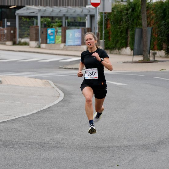 Eine Frau läuft einen Marathon, trägt ein schwarzes Shirt und Shorts, mit der Startnummer 235 auf dem Shirt. Sie läuft auf der Straße.
