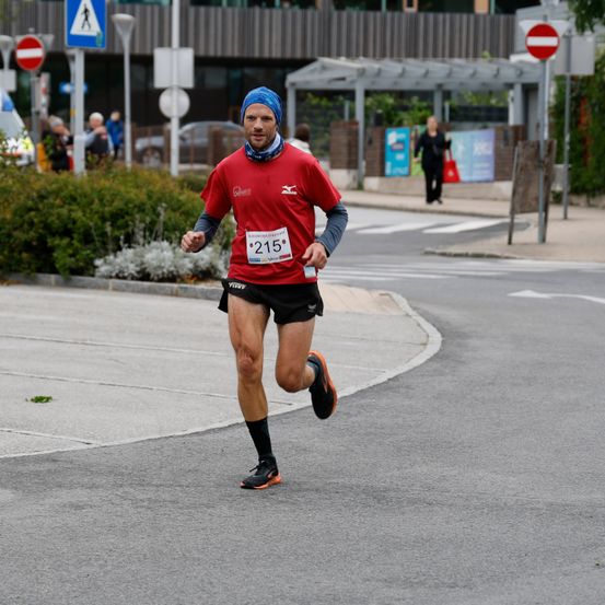 Ein Mann mit einer blauen Kopfband und einem roten Shirt mit der Nummer 215 läuft bei einem Marathon auf der Straße.