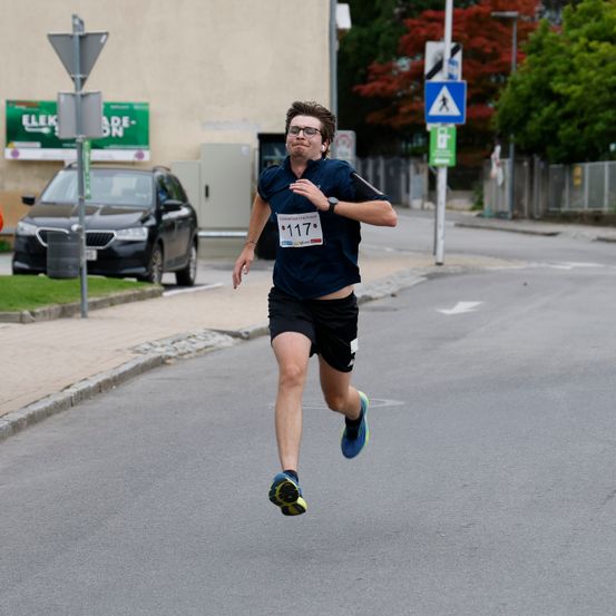 Ein Läufer mit Brille und blauem Shirt mit der Nummer 117 läuft in der Mitte der Straße.