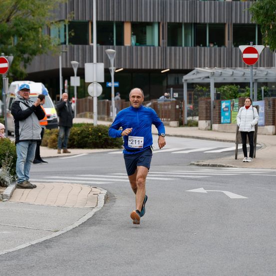 Ein Läufer in einem blauen Shirt und Shorts läuft auf einer Straße, im Hintergrund Gebäude und Bäume.