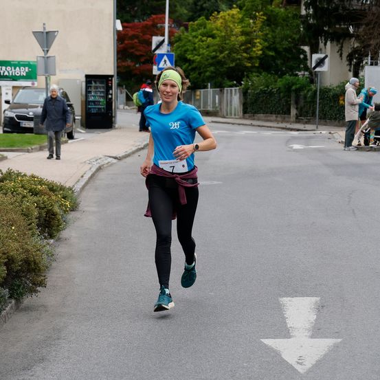 Eine Frau läuft einen Marathon mit der Nummer 7 auf ihrem Shirt, während eine Person auf dem Bürgersteig steht.
