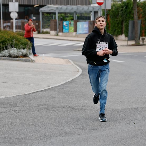 Ein Läufer mit der Nummer 218 auf seinem Shirt läuft auf einer Straße. Eine Person steht am Straßenrand.