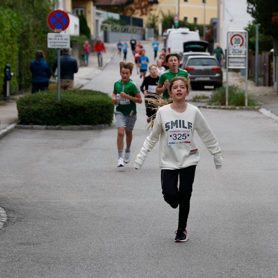 Mehrere junge Leute laufen in einem Rennen auf einer Straße. Ein Mädchen mit der Nummer 325 führt.