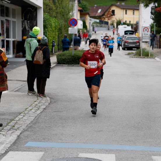 Ein Junge mit der Nummer 359 läuft in einem Marathon auf der Straße, während Menschen an der Seite stehen.