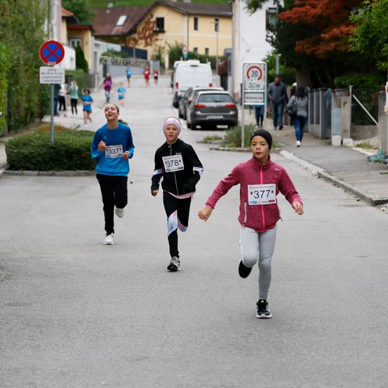 Drei Läufer nehmen an einem Rennen teil und tragen nummerierte Trikots. Die führende Läuferin trägt ein blaues Trikot mit der Nummer 337. Dahinter ist eine Läuferin in einem schwarzen Trikot mit der Nummer 378. Eine weitere Läuferin in einem rosafarbenen Trikot mit der Nummer 377 ist etwas dahinter.