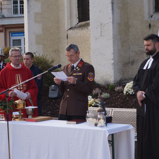 Ein Militäroffizier liest von einem Papier an einem Tisch, hinter ihm steht ein Geistlicher.