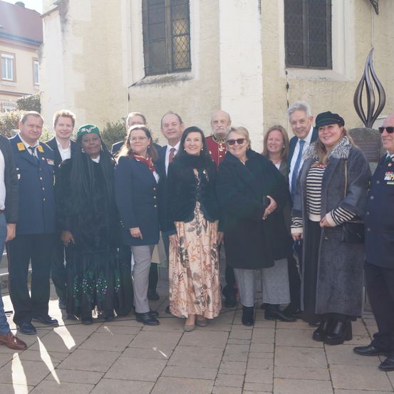 Eine Gruppe von Personen in formeller Kleidung, einschließlich Militäruniformen, steht vor einem Gebäude. Sie scheinen für ein Foto zu posieren.