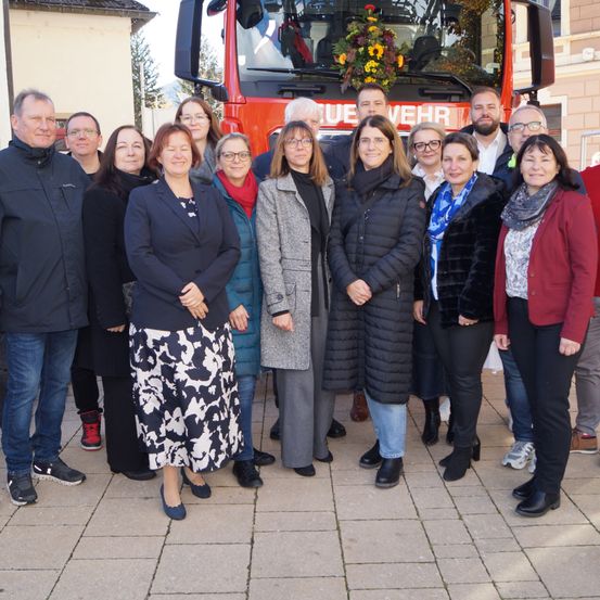 Eine Gruppe Erwachsener steht vor einem roten Feuerwehrauto mit Blumenschmuck. Sie tragen Winterkleidung und posieren für ein Foto.