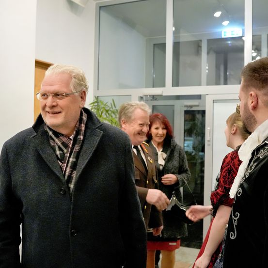 Eine Gruppe von Menschen steht in einem Flur. Ein Mann trägt eine Brille und einen karierten Schal.