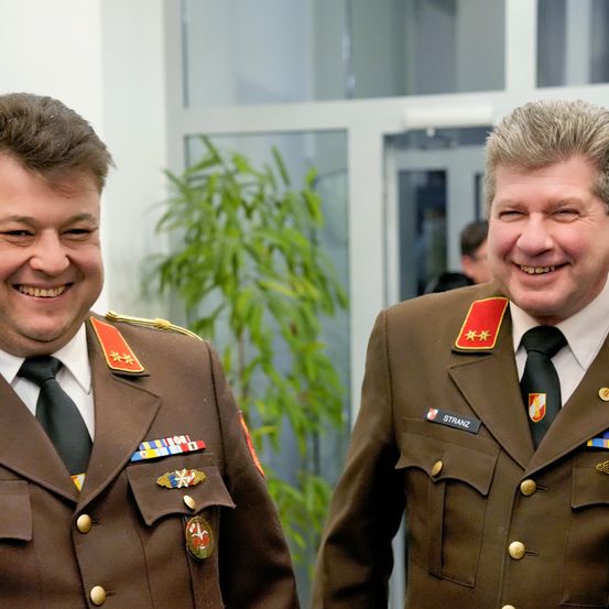 Zwei Männer in Militäruniformen lächeln in die Kamera. Sie tragen Medaillen und Abzeichen, was auf eine formelle Veranstaltung hindeutet.