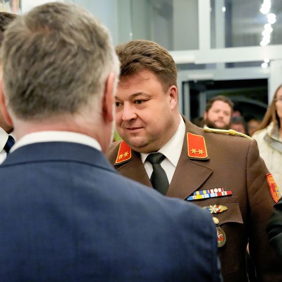 Ein Mann in Uniform führt ein Gespräch mit einem anderen Mann in einem Anzug in einem überfüllten Raum.