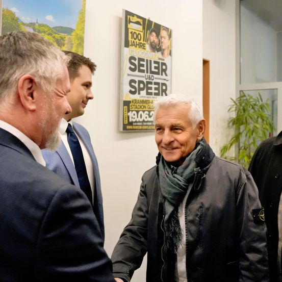 Eine Gruppe von Männern in Anzügen und Krawatten steht vor einem Plakat für ein Fußballevent.