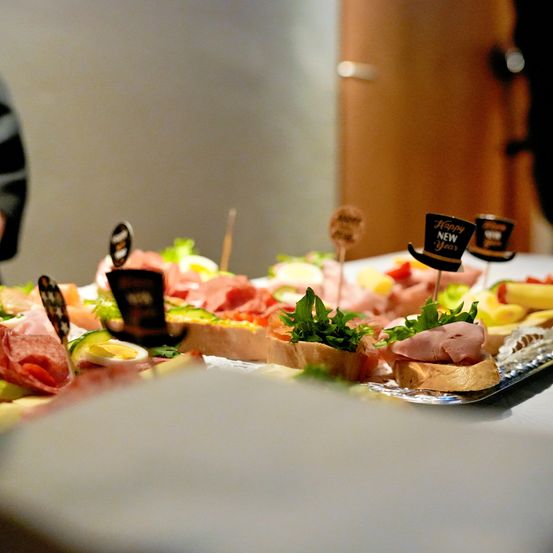 Eine Nahaufnahme eines Buffet-Tisches mit verschiedenen Speisen, darunter Fleisch, Gemüse und Brot, verziert mit dekorativen Hüten für Neujahr.