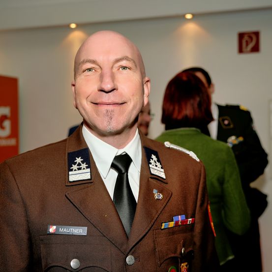 Ein lächelnder Mann in Uniform, identifiziert als Mautner, steht vor anderen in Uniform.
