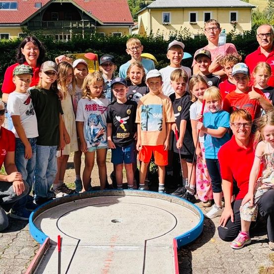 Eine Gruppe von Kindern und Erwachsenen posiert für ein Foto vor einem Minigolfplatz, einige halten Golfschläger und andere tragen Mützen.