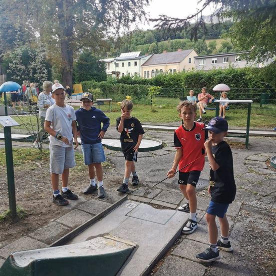 Fünf Jungen stehen auf einem Minigolfplatz. Ein Junge hält einen Golfschläger.