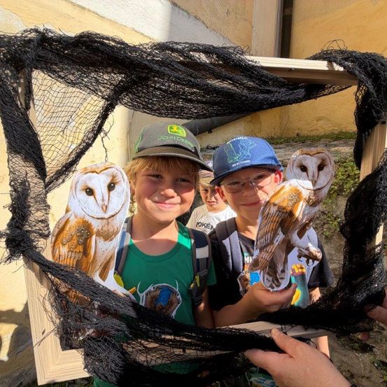 Zwei Jungen halten Ausschnitte von Eulen in einem Netz-bedeckten Rahmen und lächeln für ein Foto.