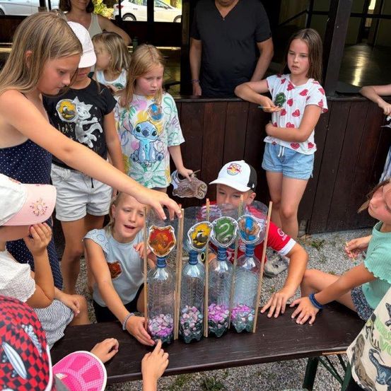 Eine Gruppe von Kindern versammelt sich um einen Tisch mit Flaschen, die mit Süßigkeiten gefüllt sind, wahrscheinlich an einem Spiel oder einer Aktivität teilnehmend.