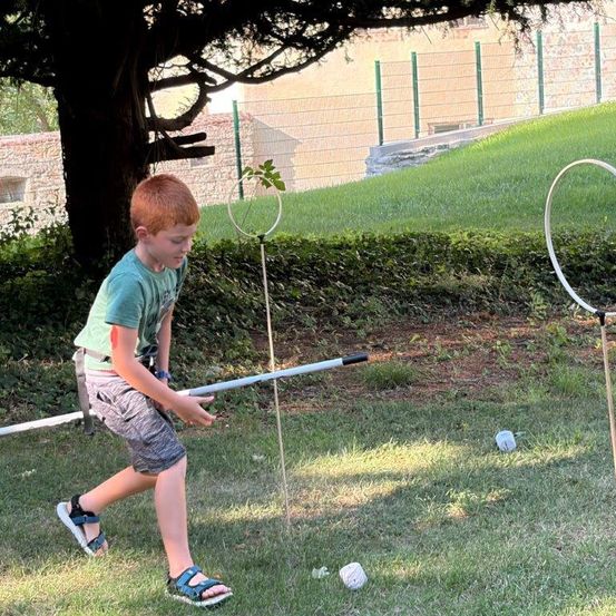 Ein junger Junge in einem grünen T-Shirt und Sandalen spielt ein Golfspiel auf einem Rasenfeld mit zwei weißen Reifen als Zielen.