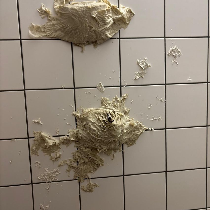 Eine weiße geflieste Wand mit verschiedenen Gipsstücken, die herumliegen, möglicherweise von einer Renovierung oder Beschädigung.