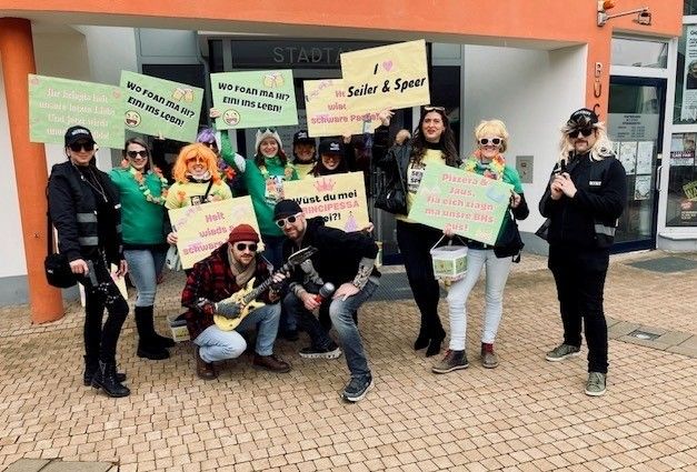 Eine Gruppe von Menschen in grünen Kostümen posiert für ein Foto vor einem Gebäude mit Schildern und Gitarren.