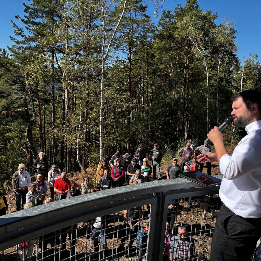 Ein Mann hält eine Rede in einem Wald vor einer Menschenmenge.