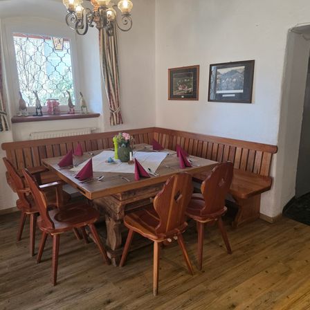 Ein gemütlicher Essbereich mit Holzmöbeln, einschließlich Tisch, Stühlen und einer Bank, geschmückt mit Blumendekor und gerahmten Bildern an der Wand.