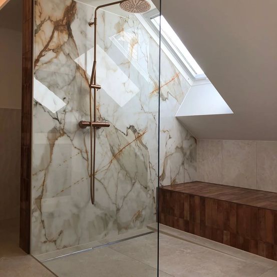 Ein luxuriöses Badezimmer mit einer Glasdusche, Marmorwänden und einer Holzbank, ergänzt durch ein Dachfenster für natürliches Licht.