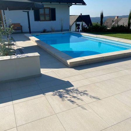 Ein Swimmingpool im Garten mit einem gefliesten Boden und einer Bank in der Nähe eines Hauses.