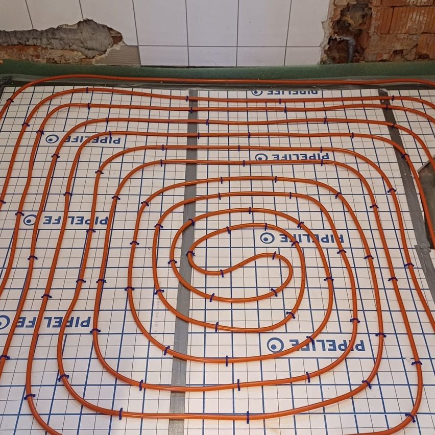 Ein Raster orangefarbener Rohre ist auf einem weißen Fliesenboden installiert. Jedes Rohr ist mit blauem Text beschriftet, der 'PTFE' liest. Die Rohre bilden ein Zickzackmuster.