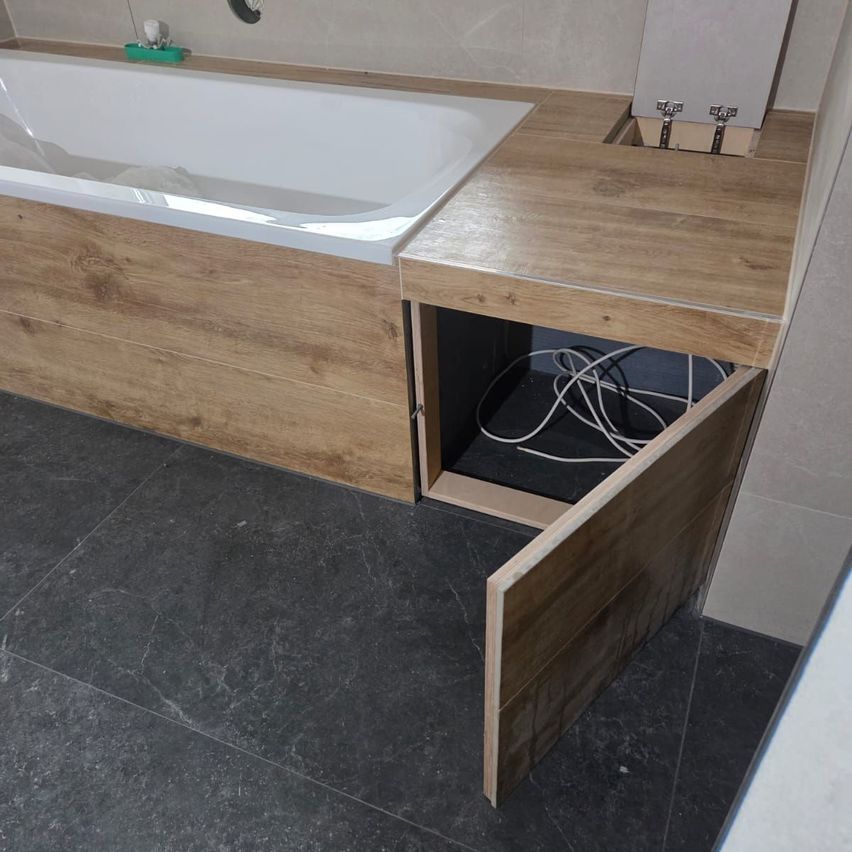 A modern bathroom with a large bathtub, wooden countertop, and exposed electrical outlets. The floor is tiled with black marble.