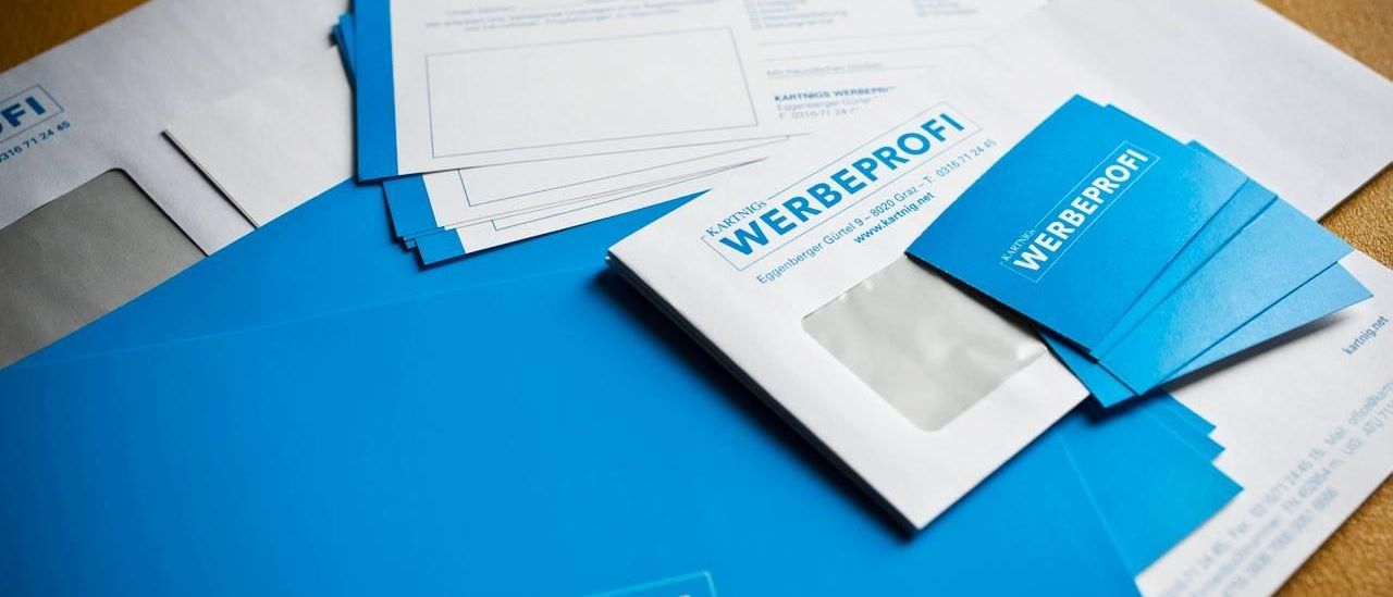 Mehrere blaue Umschläge mit dem Wort Werbeprofi, auf einer Holzoberfläche platziert.