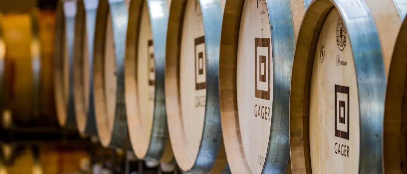 Eine Reihe von Holzfässern mit Metallbändern und Logos, die in einem Raum, möglicherweise in einem Weingut, gestapelt sind.