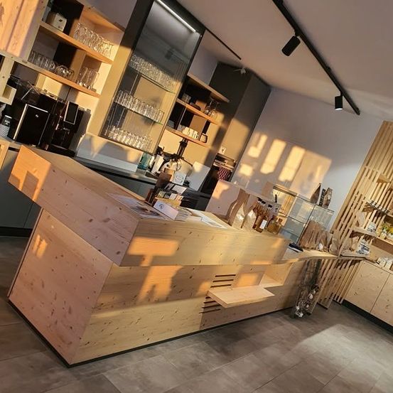 Eine Holztheke in einem Café mit Regalen und Glasvitrinen dahinter. Die Theke wird von Sonnenlicht beleuchtet.