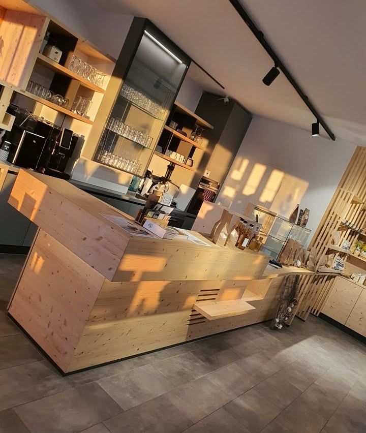 Eine Holztheke in einem Café mit Regalen und Glasvitrinen dahinter. Die Theke wird von Sonnenlicht beleuchtet.