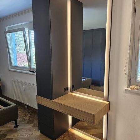 Ein modernes Innendesign mit einem großen Spiegel, einem Holzschreibtisch und einem blauen Kleiderschrank. Der Raum hat einen Holzboden und eine weiße Wand.