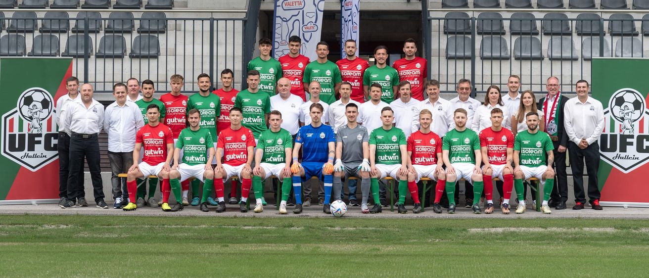 Eine Fußballmannschaft posiert für ein Gruppenfoto vor einem Stadion, mit Spielern in grünen, roten und weißen Trikots.