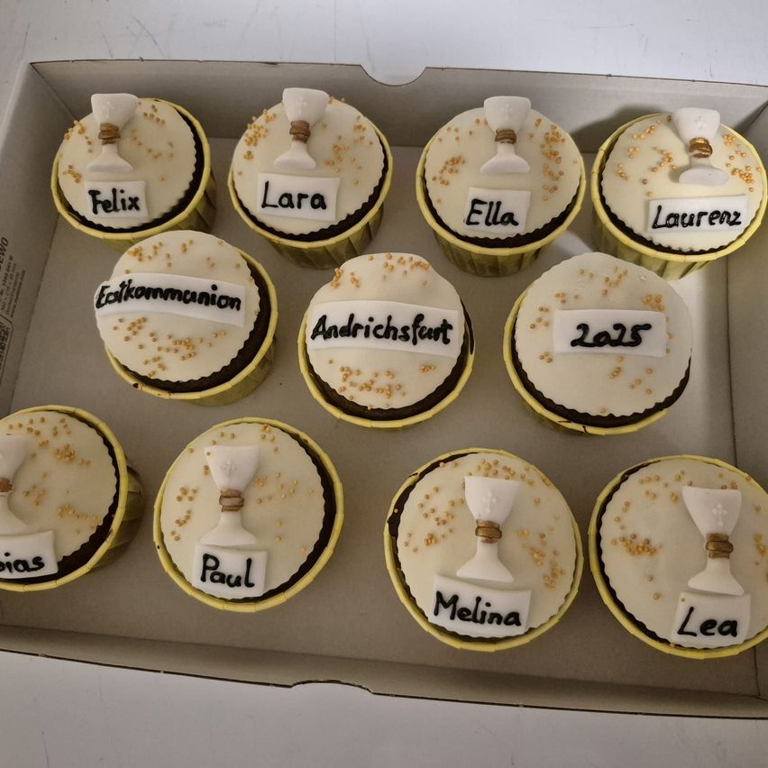 Eine Schachtel mit neun Cupcakes, jeweils mit einer weißen Zuckergussspitze mit einem Kelch und goldenen Punkten. Die Cupcakes tragen Namen wie Felix, Lara, Ella, Lauren, Paul, Melina und Lea.