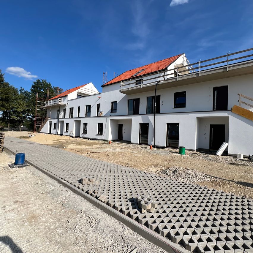 Ein Baugelände mit einer Reihe moderner weißer Gebäude unter blauem Himmel. Ein Gebäude hat ein rotes Dach.
