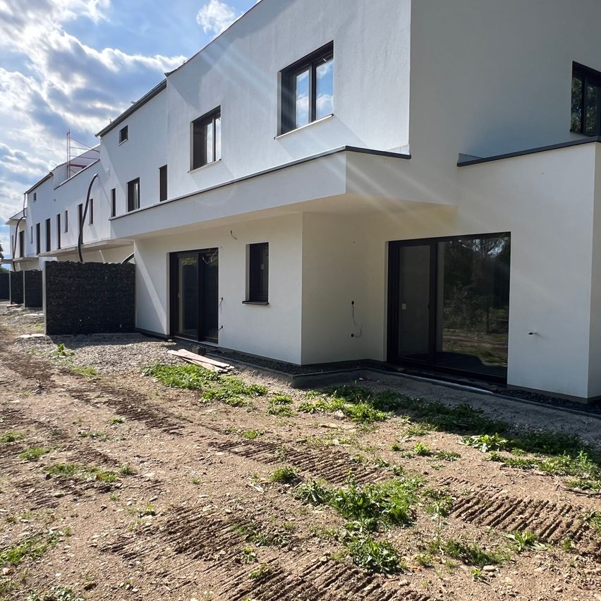 Ein modernes weißes Haus mit großen Fenstern und Glastüren befindet sich teilweise im Bau. Die Vorderseite hat eine Kiesauffahrt mit einigen Grasflecken.