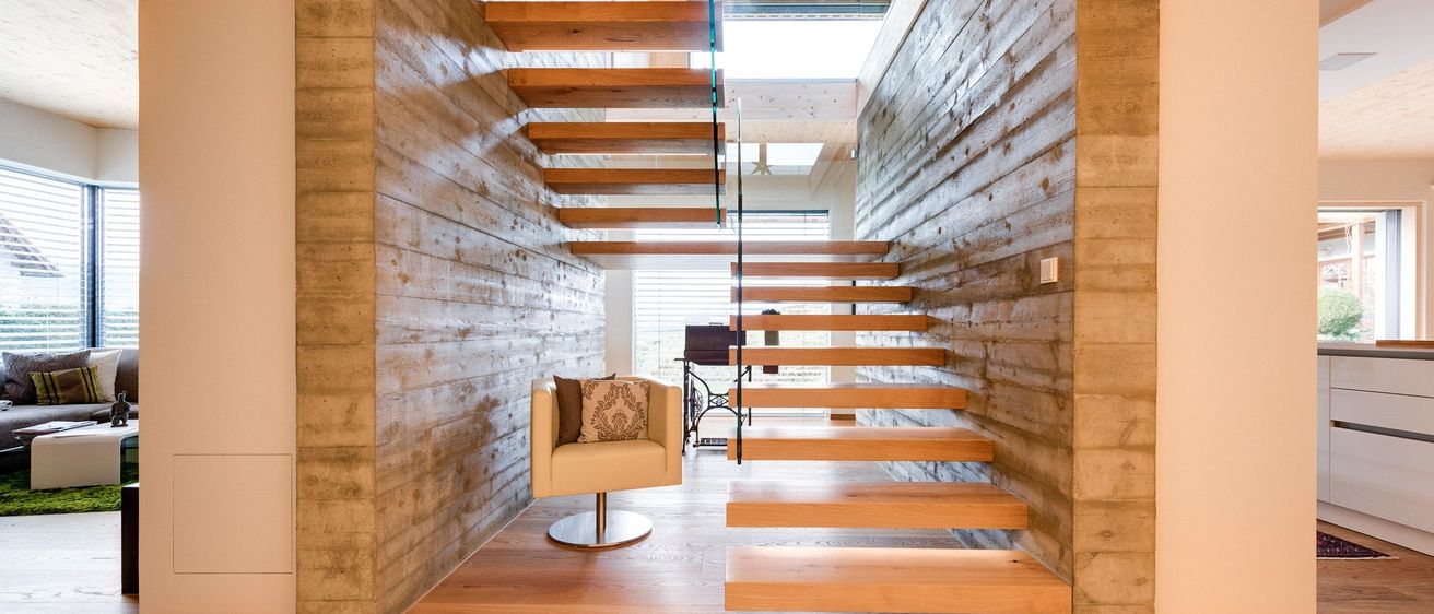 Eine moderne Treppe mit Holzstufen und Glasgeländern ist sichtbar, mit einem gemütlichen Sessel in der Nähe. Holzwände und eine Glasdecke sind vorhanden.