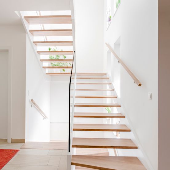 Eine moderne, weiße Treppe mit Holzstufen und einem Glasgeländer führt in die obere Etage. Die Treppe hat ein minimalistisches Design mit einem schlanken, modernen Look.
