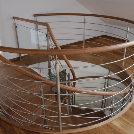 Eine moderne Wendeltreppe mit hölzernen Handläufen und Metallstützen. Die Treppe führt hinunter zu einem Holzboden.