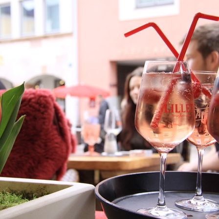 Ein Tisch mit drei Weingläsern gefüllt mit Wein, zwei mit roten Strohhalmen, einem roten Hut und einer Tulpe in einem weißen Topf.