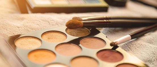 Ein Make-up-Palette mit verschiedenen Lidschatten-Nuancen und einem Pinsel auf einem weißen Tuch.
