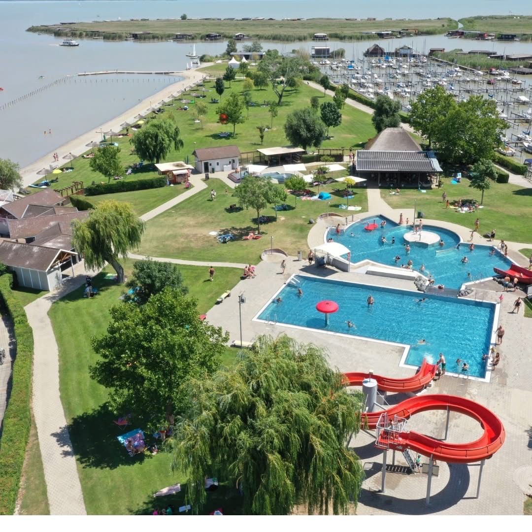 Ein Luftbild eines Feriengebiets mit Schwimmbad, Wasserrutsche, Rasenfläche, mehreren Häusern, Bäumen und einem Boot, das auf dem See fährt.
