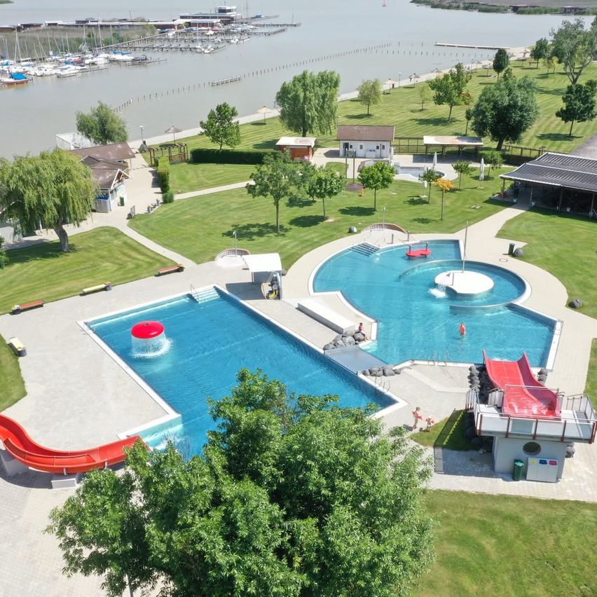 Ein Luftbild eines Freizeitbereichs mit einem großen Schwimmbad, einer Rutsche und einem See im Hintergrund.
