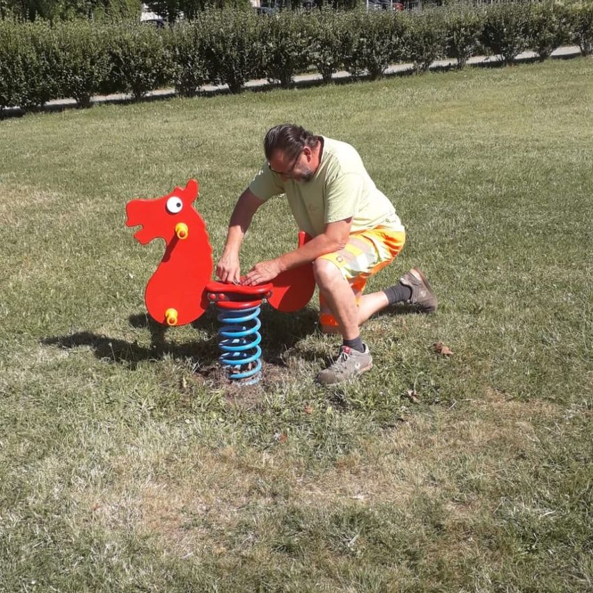 Ein Mann kniet auf einem pferdeförmigen Feder im Park und hält die Feder mit beiden Händen.