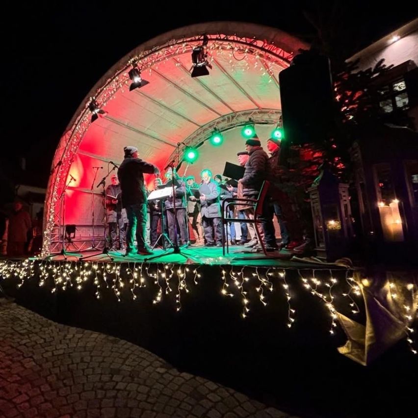 Eine Gruppe von Menschen steht mit Lichtern und Mikrofonen auf der Bühne und singt vor einem Publikum.